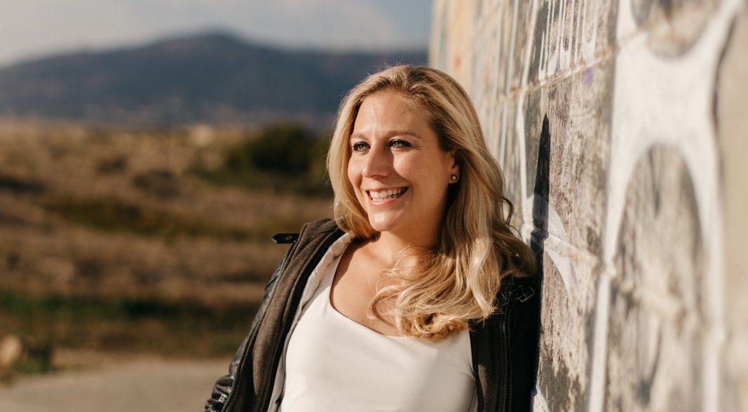 Sina Heider lehnt lachend an einer bemalten Mauer, im Hintergrund Berge